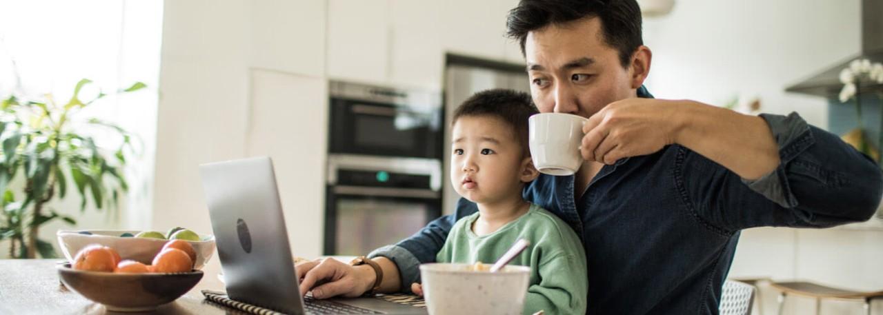 man working on the computer while drinking coffee with his son