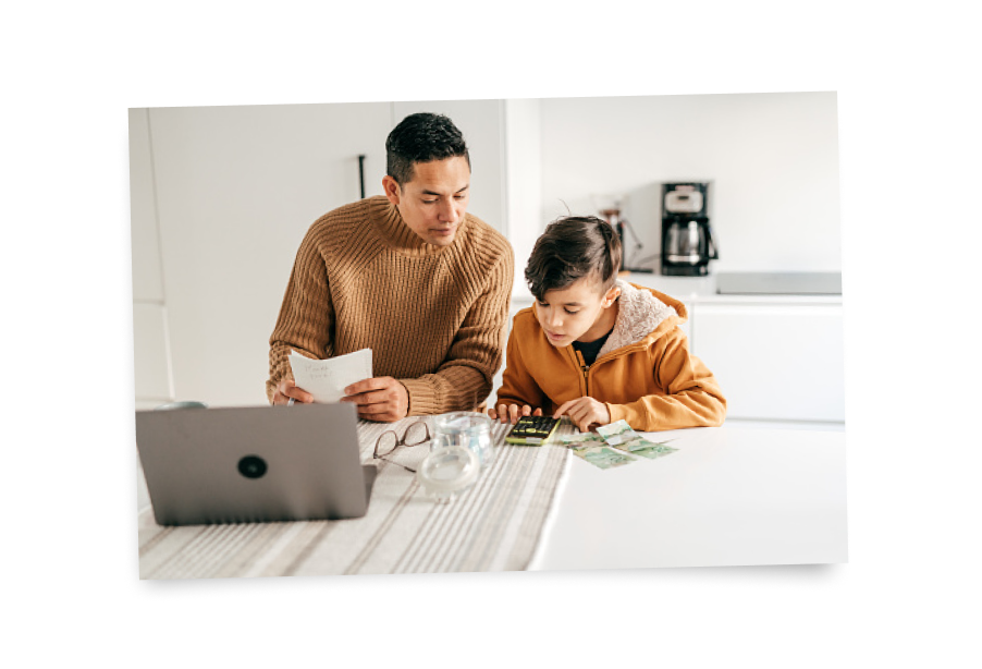 image of dad and son using computer and calculator, jar of money and papers on side